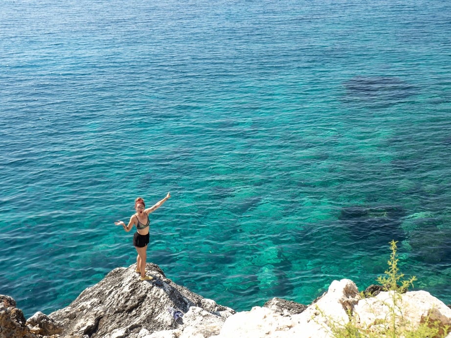 a solo female traveller pointing at a very blue sea