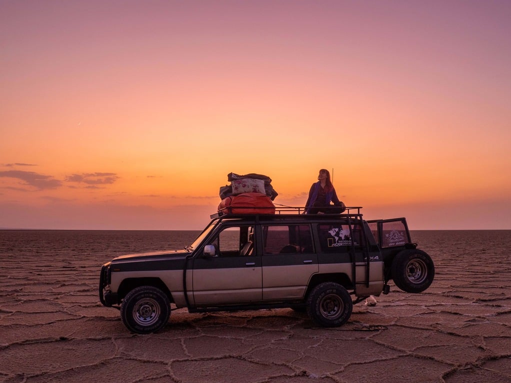 solo female traveller on top of a jeep in front of sunset