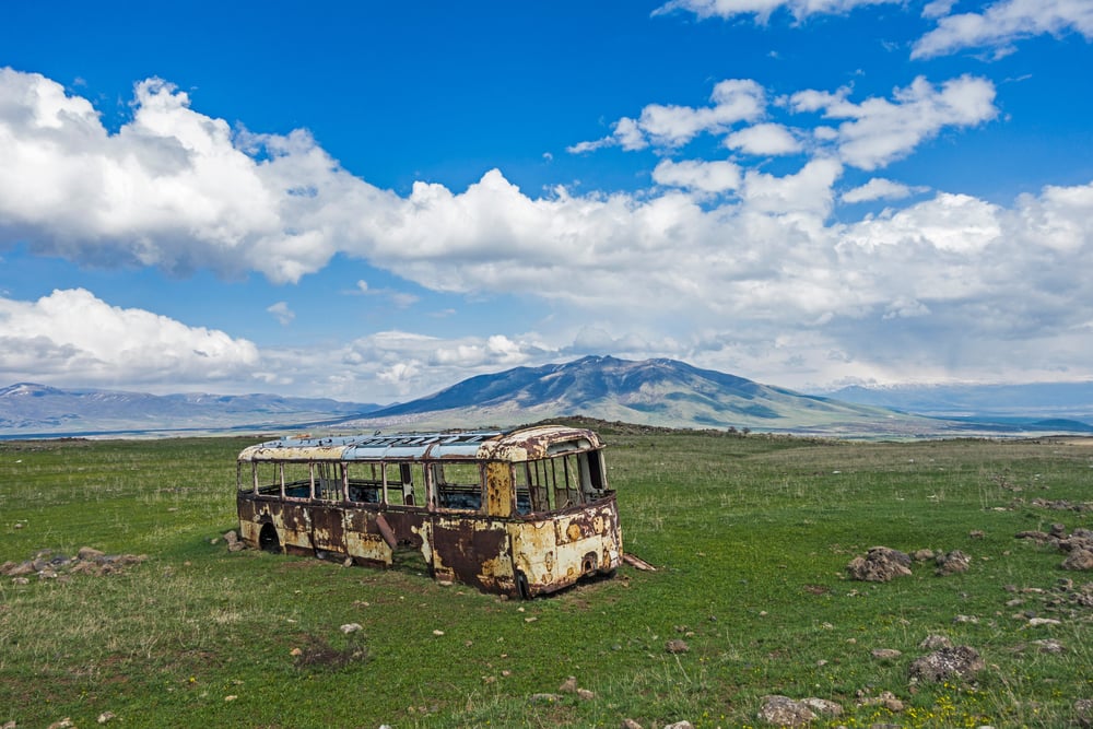 在亚美尼亚的一片田野上，废弃的旧公共汽车，背景是一座山