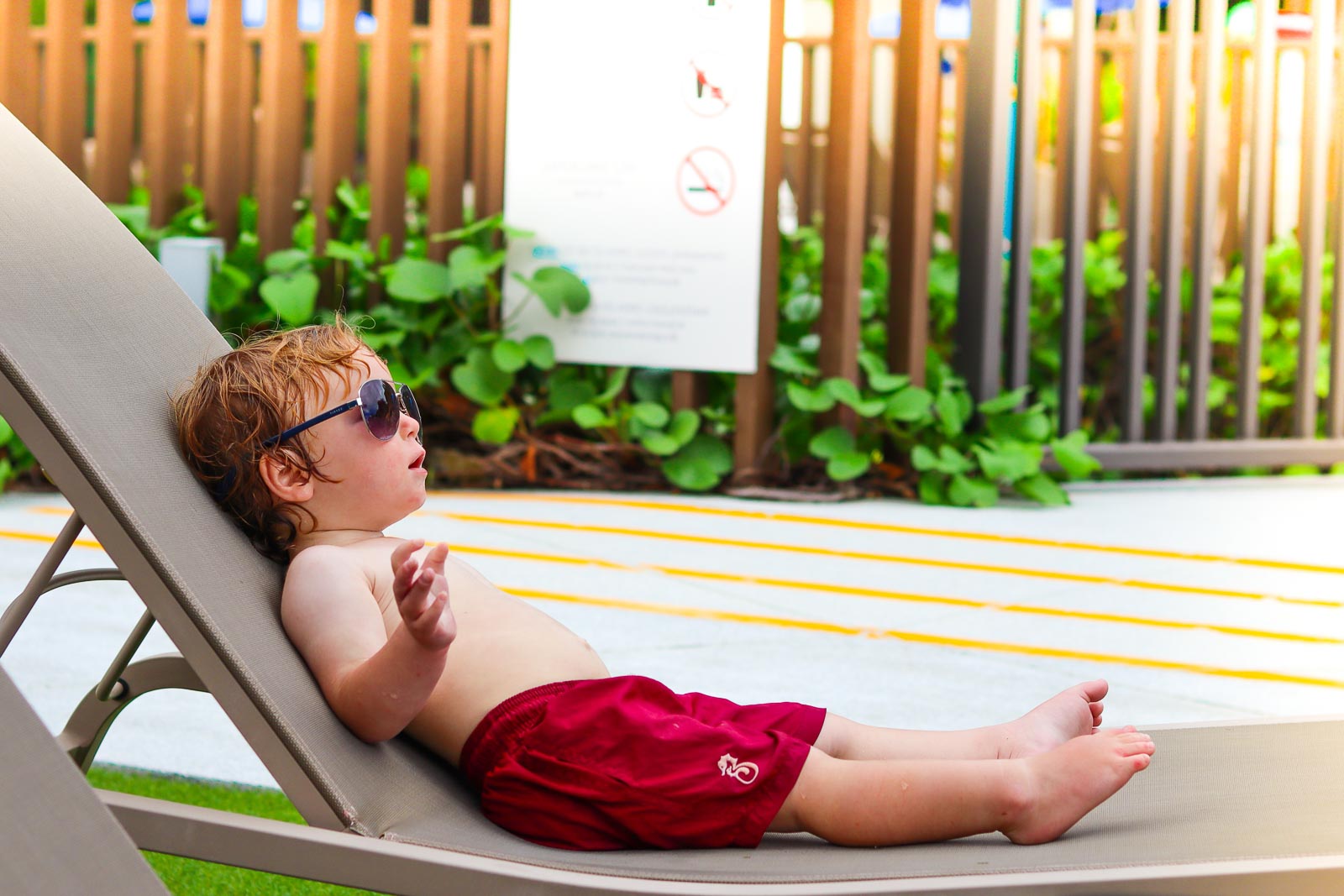 孩子戴着太阳镜，坐在躺椅上，在一个温暖的地方全职家庭旅行