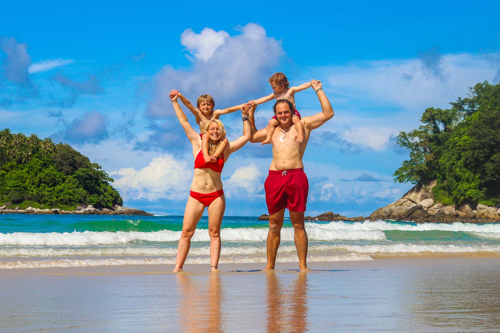 一对夫妇站在迷人的热带海滩上，肩上各扛着一个孩子