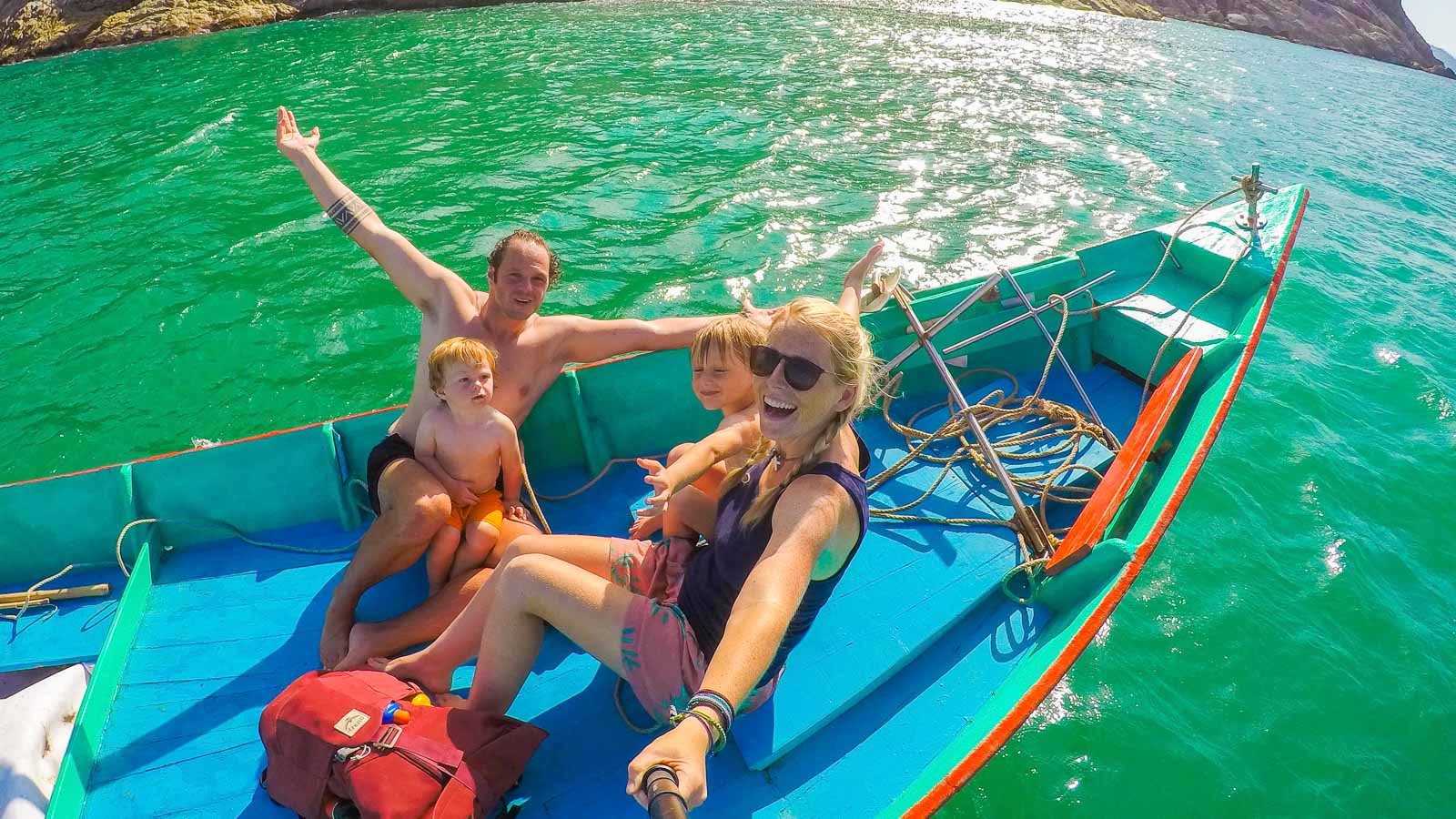泰国，一家人坐在蓝绿色水面上的蓝色小船上