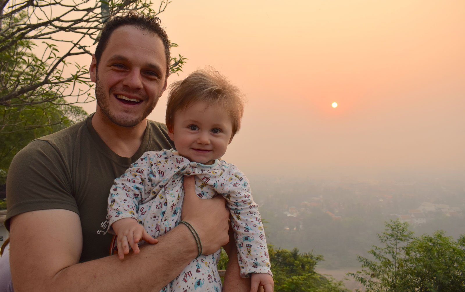 男子抱着一个孩子在橙色日出前在老挝全职家庭旅行