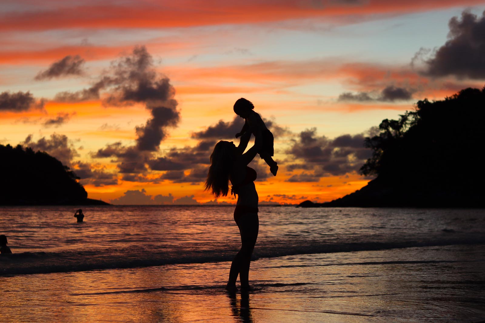在沙滩上，一个女人抱着一个婴儿，在一个虚幻的橙色和粉红色的日落中